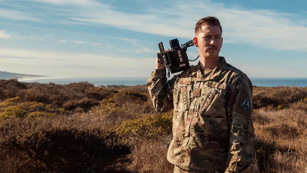 a military photographer stands, holding a camera